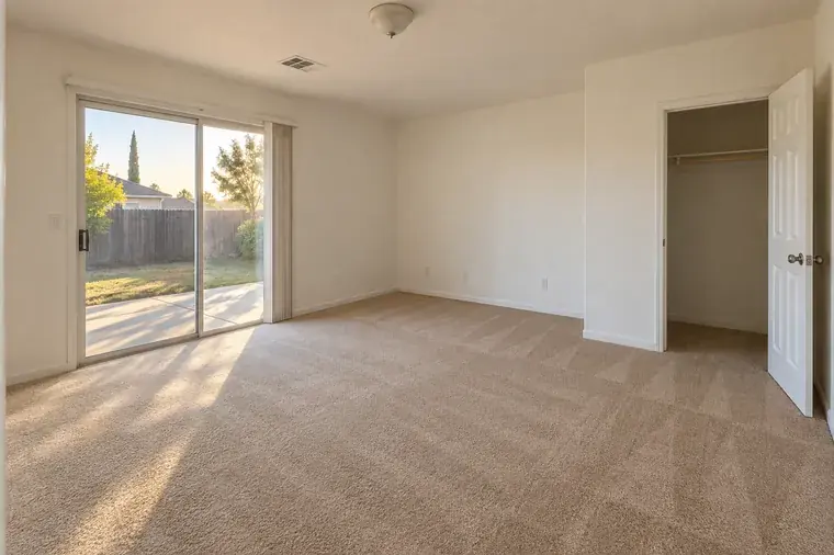 Empty carpeted bedroom with a sliding glass door, cleaned and ready for move-in